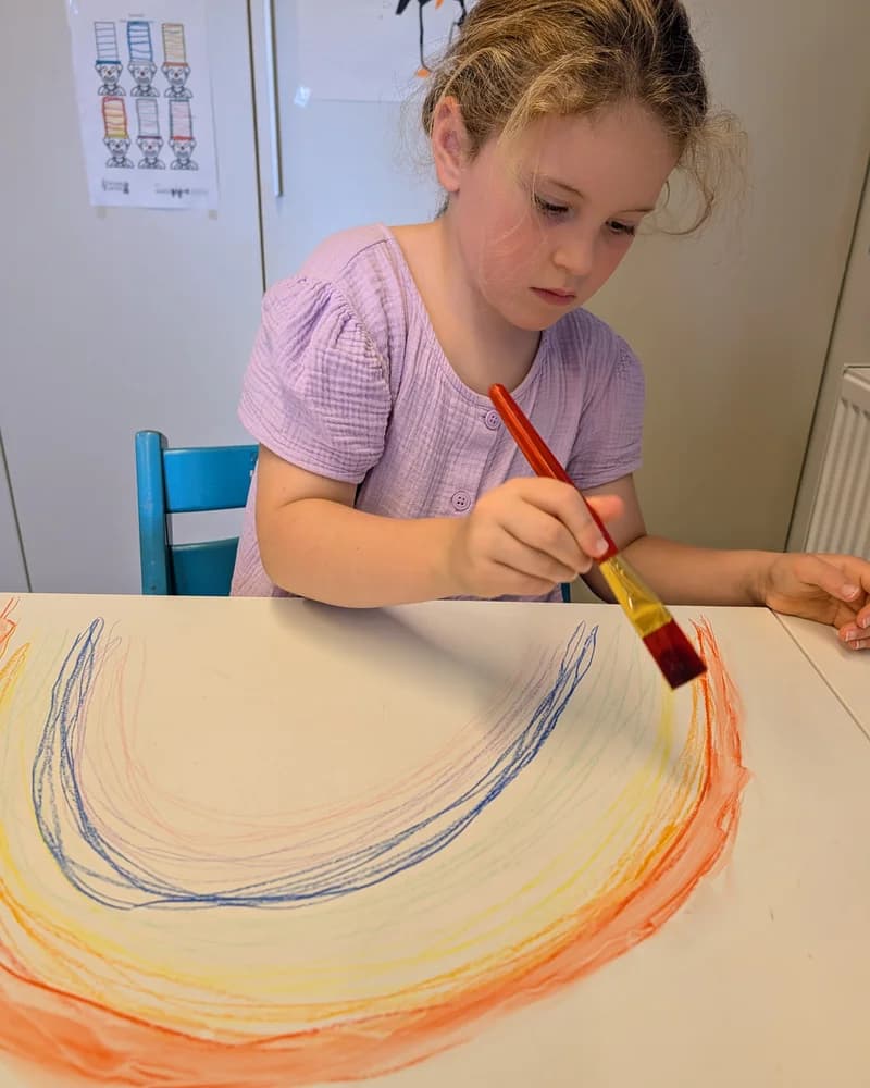 Kind schildert geconcentreerd een kleurrijke regenboog tijdens een sessie rond fijne motoriek